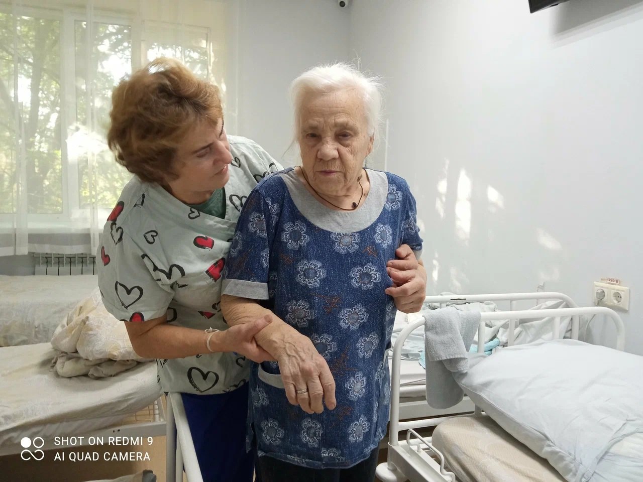 Сотрудник помогает пожилой пациентке передвигаться